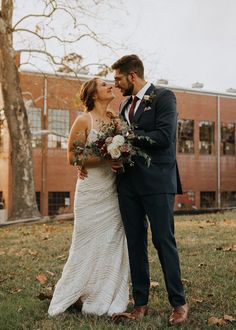 a bride and groom kissing in front of a brick building on their wedding day at the park