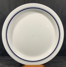 an empty white plate with blue stripes on the rim sits on a wooden stand against a black background