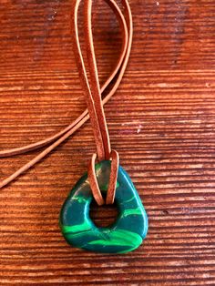 a necklace with a green and blue pendant on a brown leather cord sitting on top of a wooden table