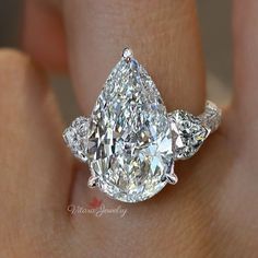 a woman's hand holding an engagement ring with two pear shaped diamonds