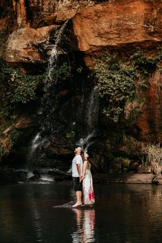 a man and woman standing in front of a waterfall