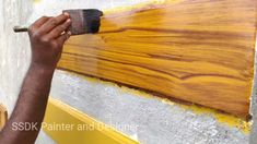 a man painting wood with yellow paint on the side of a wall and holding a brush