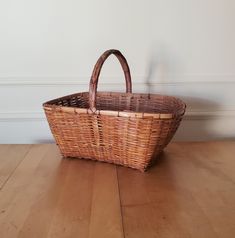 a brown wicker basket sitting on top of a wooden floor next to a wall