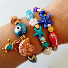 Beautiful handmade bracelets with Greek Porcelain beads, golden charms and very summery.  Here you have your looks ready for the holidays and for the whole summer.  I present you the trends in bracelets and very colorful jewelry for this summer. Ideal to wear alone or combine them with other summer jewelry.  In addition to being beautiful, they are great to carry good luck with you every day. Sold separately, choose the bracelet or bracelets you like best from the drop-down menu and show off a g Handmade Charm Bangle For Beach, Handmade Bangle Charm Bracelet For Beach, Bohemian Evil Eye Jewelry For Vacation, Handmade Charm Bracelet For Beach, Handmade Mediterranean Jewelry For Gift, Bohemian Charm Bracelets For The Beach, Bohemian Beach Bracelets With Charms, Handmade Evil Eye Bracelet With Round Beads For Beach, Handmade Gold Evil Eye Bracelet For Beach