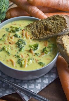 a bowl of broccoli soup with bread and carrots