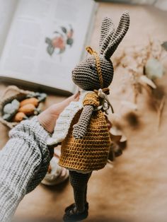 a crocheted bunny doll is held up by someone's hand in front of an open book