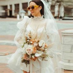 a woman in a white wedding dress and sun glasses is standing on the side walk