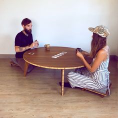 a man and woman sitting at a wooden table playing the game monopoly on their phones