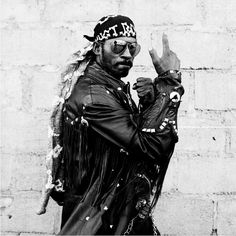 a man in leather jacket and hat giving the peace sign