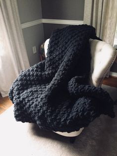 a black crocheted blanket sitting on top of a white chair next to a window