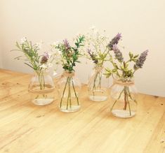 three clear vases with flowers in them on a wooden table top, one is empty