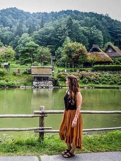 a woman standing on the side of a road next to a lake with houses in the background