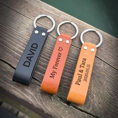 three personalized leather keychains are sitting on a wooden table, one is for dad and the other is for daughter