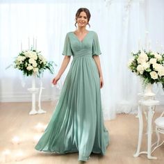 a woman in a green dress standing next to some white flowers and candles on a table