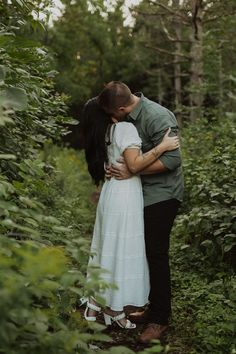 a man and woman kissing in the woods with their arms around each other as they stand next to each other