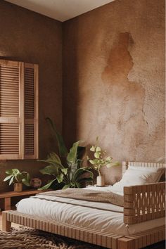 a bed sitting next to a window with shutters on each side and a plant in the corner