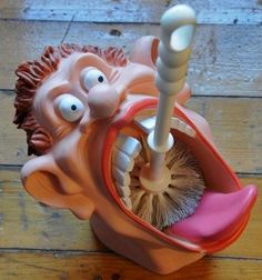 an odd looking toothbrush holder on a wooden floor with eyes and tongue sticking out