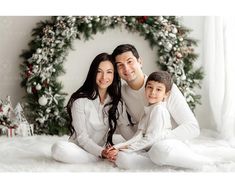 a man, woman and child sitting on a bed in front of a christmas wreath