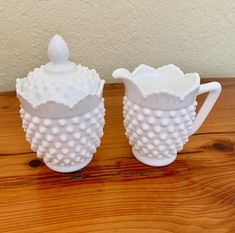 two white vases sitting on top of a wooden table