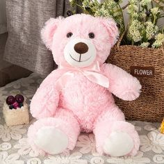 a pink teddy bear sitting next to a basket with flowers