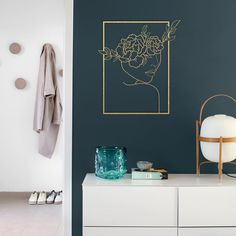 a white dresser topped with a vase filled with flowers next to a wall mounted art piece