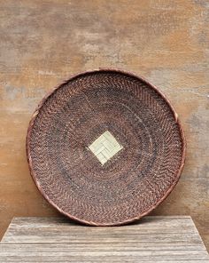 a brown basket sitting on top of a wooden table next to a wall with a white square in the middle