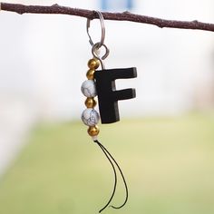 the letter f is hanging from a t - shaped beaded necklace on a tree branch