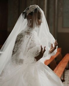 a woman in a white wedding dress standing next to a bench with her hands together