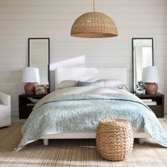 a bedroom with a bed, mirror and two lamps hanging from the ceiling above it