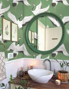 a bathroom with green wallpaper and white birds painted on the walls, along with a round mirror