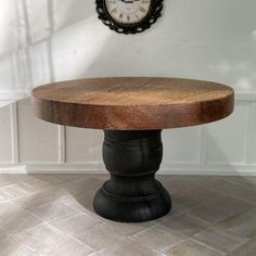 an old wooden table with a clock on the wall behind it in a white walled room