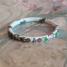 This is a vintage cloisonne bracelet. It is white floral with gold trim. This piece has a hinge and pulls open. There is a chip in the bracelet as you can see in the images as well as specks/pockmarks on the piece. The price reflects this. All sales are final.  The bracelet measures a hair under 2.5 inches across on the interior.  If you have a wish list or are looking for something specific, please ask. I may have exactly what you are looking for. As always please convo me with any questions or concerns regarding this item or with any international shipping questions. Unfortunately I do not accept returns or grant refunds. All shipping fees include handling fees. If you would like to combine shipping costs for more than one item, I would be happy to do so if you convo me before purchase. Antique White Bracelet Jewelry, White Antique Bracelet Jewelry, White Antique Bracelet, Collectible White Bracelet Jewelry, Vintage White Hand Painted Jewelry, Vintage Hand Painted White Jewelry, Vintage White Bracelets For Wedding, Vintage Hand Painted Bracelets As Gift, Vintage Enamel Bangle As A Gift