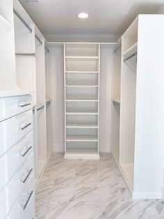 an empty walk in closet with white cabinets and marble flooring on the side wall