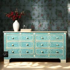 a vase with flowers on top of a blue and white dresser in front of a floral wallpaper