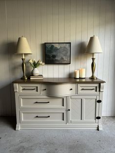 a white dresser with two lamps on top of it