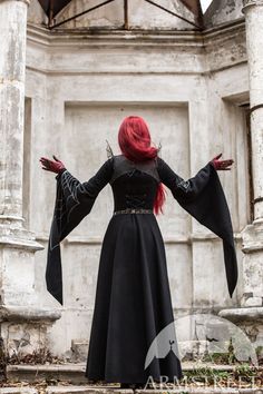 a woman with red hair and black dress standing in front of an old white building