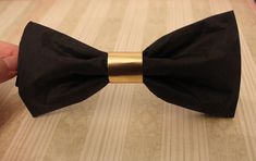 a hand holding a black bow tie on top of a wooden table next to a gold bar