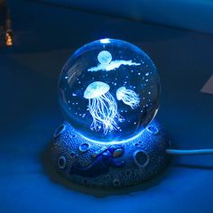 a glass ball with jellyfish in it sitting on a blue surface next to an electrical outlet