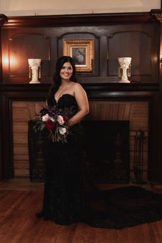 a woman standing in front of a fire place holding a bouquet of red and white flowers