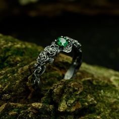 a close up view of a ring with green stone in the middle on mossy rocks