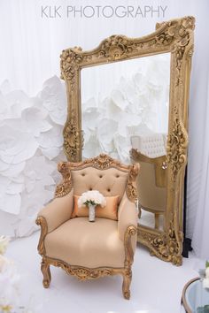 a chair sitting in front of a large mirror with flowers on the floor next to it