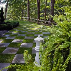 a checkered chess board in the middle of a garden with trees and bushes around it