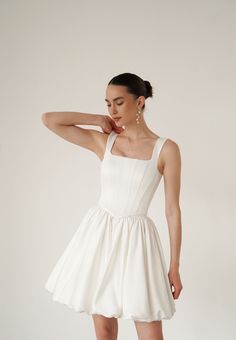 a woman in a short white dress posing for the camera with her hand on her head