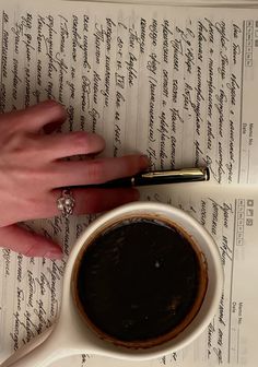 a person's hand resting on top of a cup of coffee next to an open book