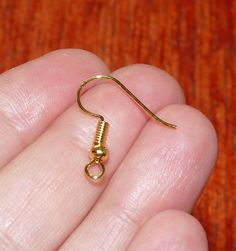 a person holding a tiny gold earring in their left hand and wearing it as a hook