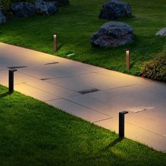 some lights that are on in the grass near bushes and rocks, along with two benches