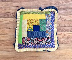 a patchwork pillow sitting on top of a wooden floor covered in blue and yellow fabric