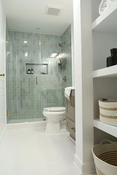 a white toilet sitting in a bathroom next to a walk in shower and shelves filled with baskets