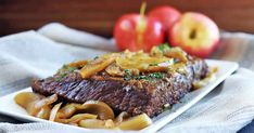 a white plate topped with meat covered in mushrooms next to an apple on top of a table