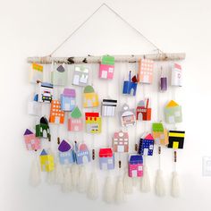 a group of colorful houses hanging from a wooden stick on a wall next to tassels